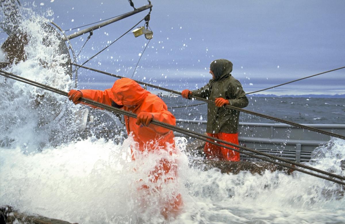 Alaska. Commercial fishing boat crew members help wind in the cables on The Dawn trawler during a Pollock opener out of Kodiak. Rough seas.