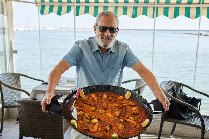 Senior grey haired man smiling confident holding seafood paella at coffee shop terrace