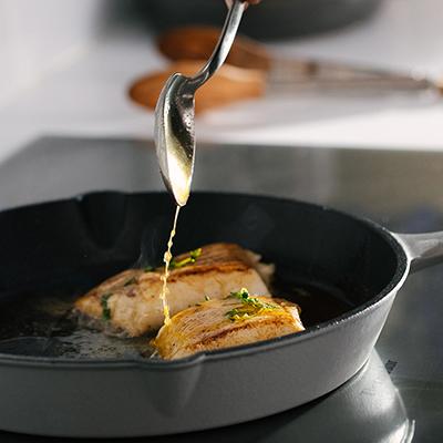 Recipes for lent with a cast iron skillet full of sea bass fillets with a spoon drizzling butter over the top.