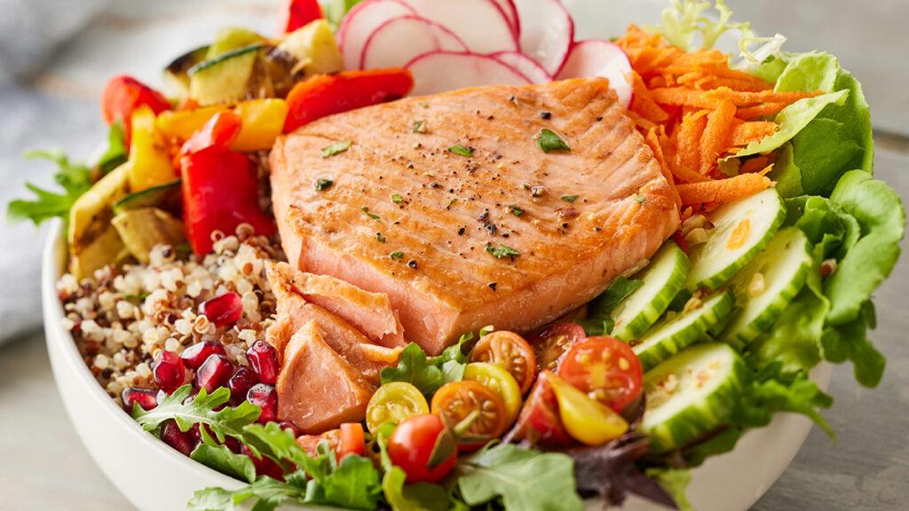 Vitamins in fish with a bowl of salmon, quinoa, and vegetables.