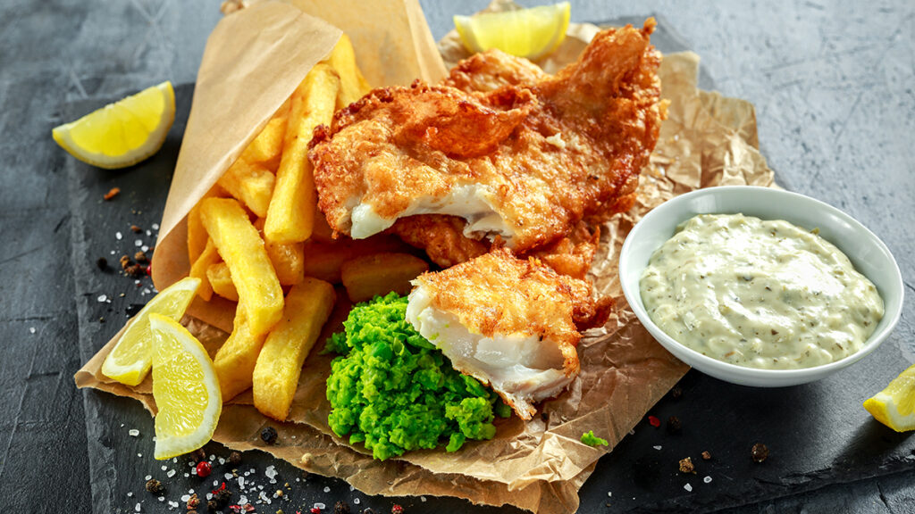 British Traditional Fish and chips with mashed peas, tartar sauce on crumpled paper.