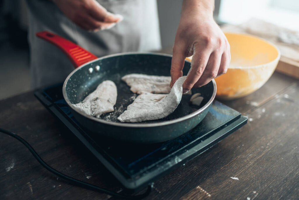 Chef cooking sea bass fish fillet on a frying pan