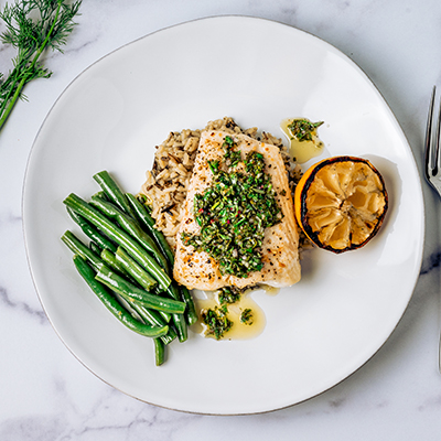 Top view of halibut fish with chimichurri sauce green beans lemon on a white plate on marble table