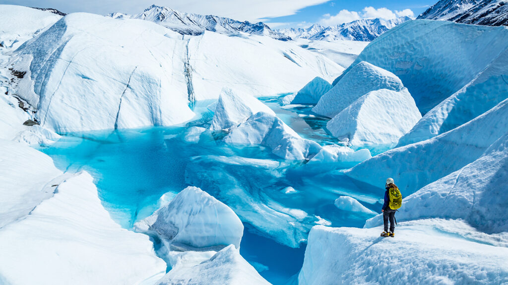 Young woman standing near deep blue lake on the Matanuska Glacier